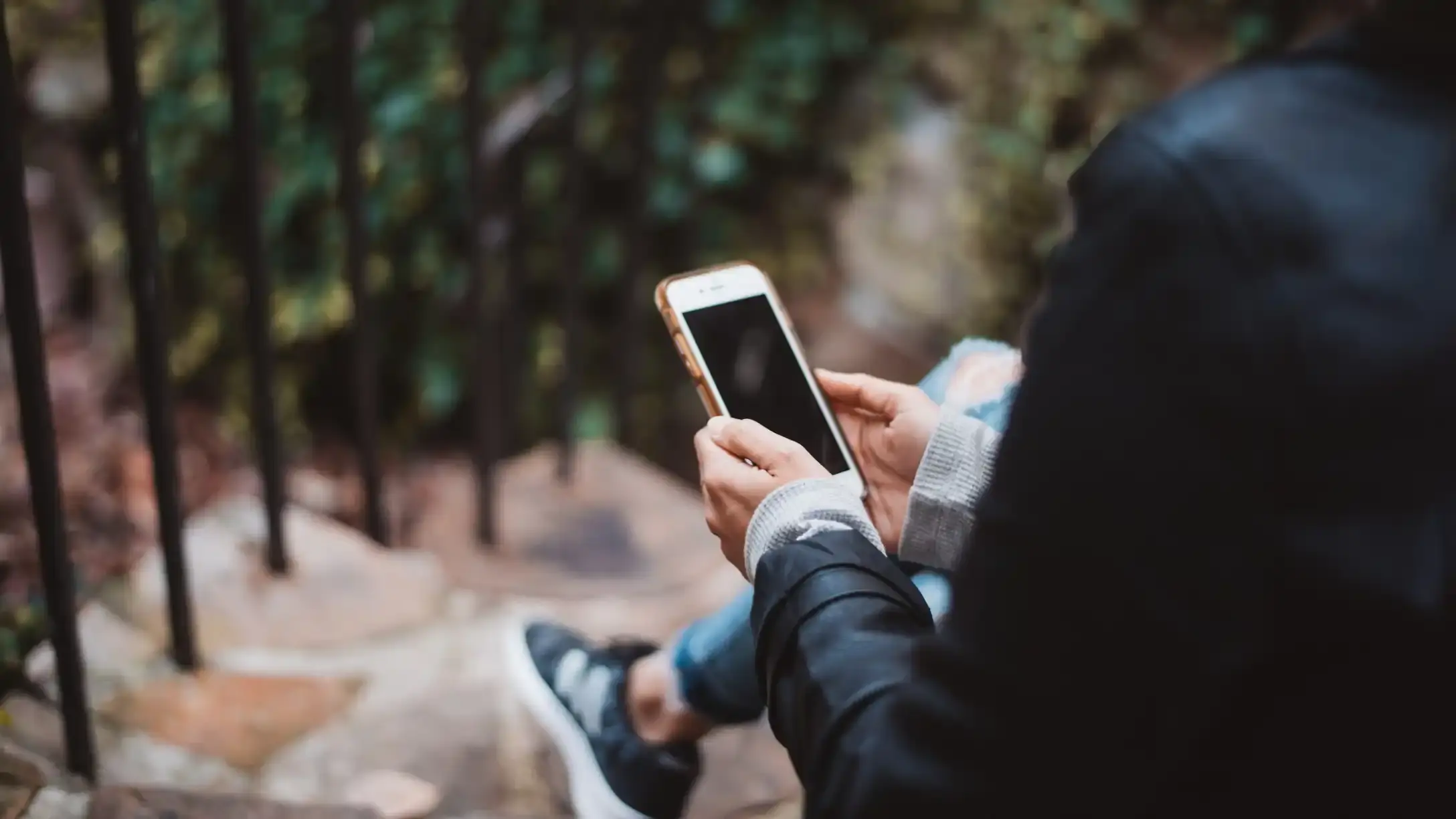 An over the shoulder shot of a woman sat on a step holding a smartphone