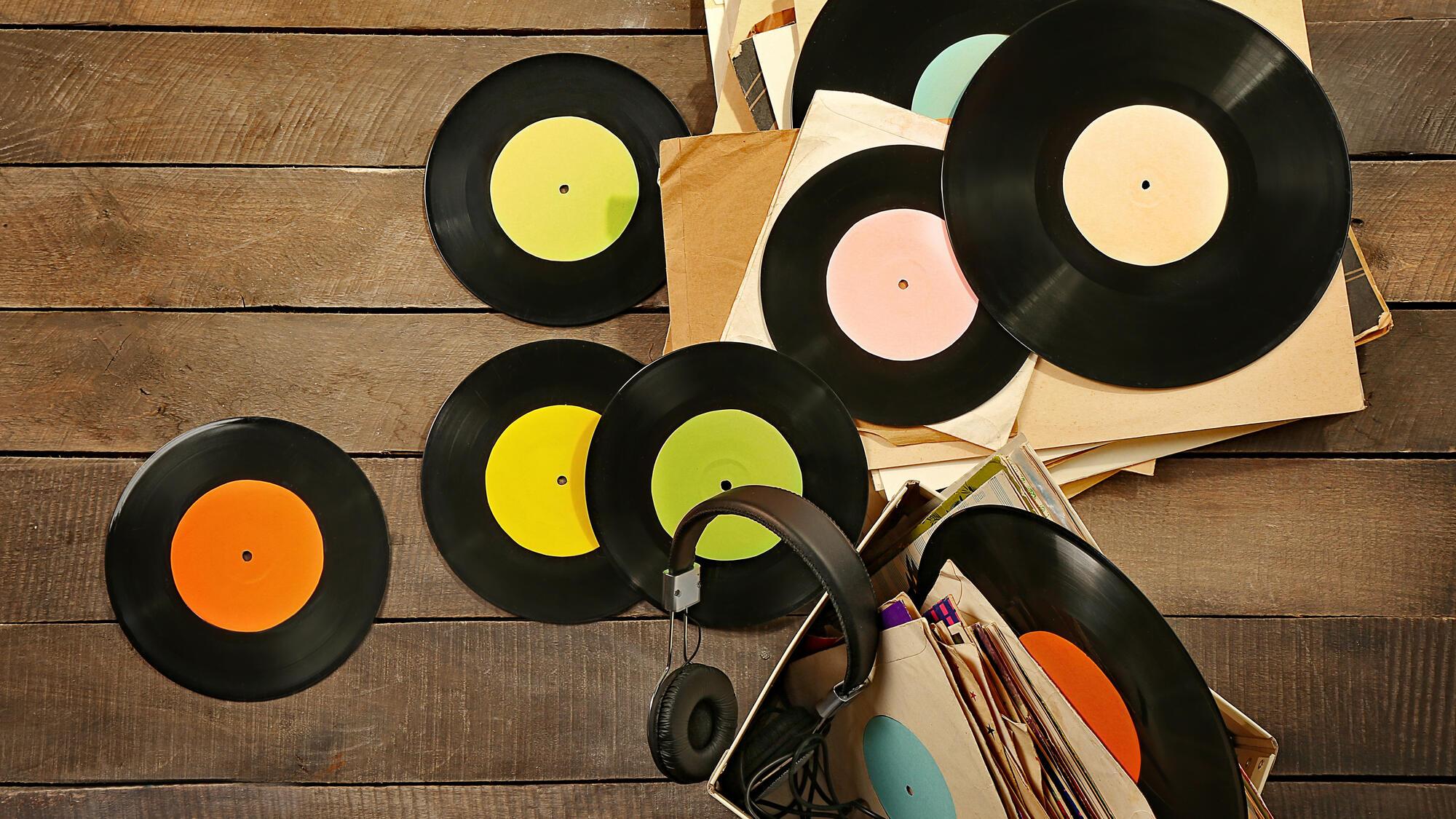 Scattered records and a box of records with a headset, on a wooden floor from a birdseye view