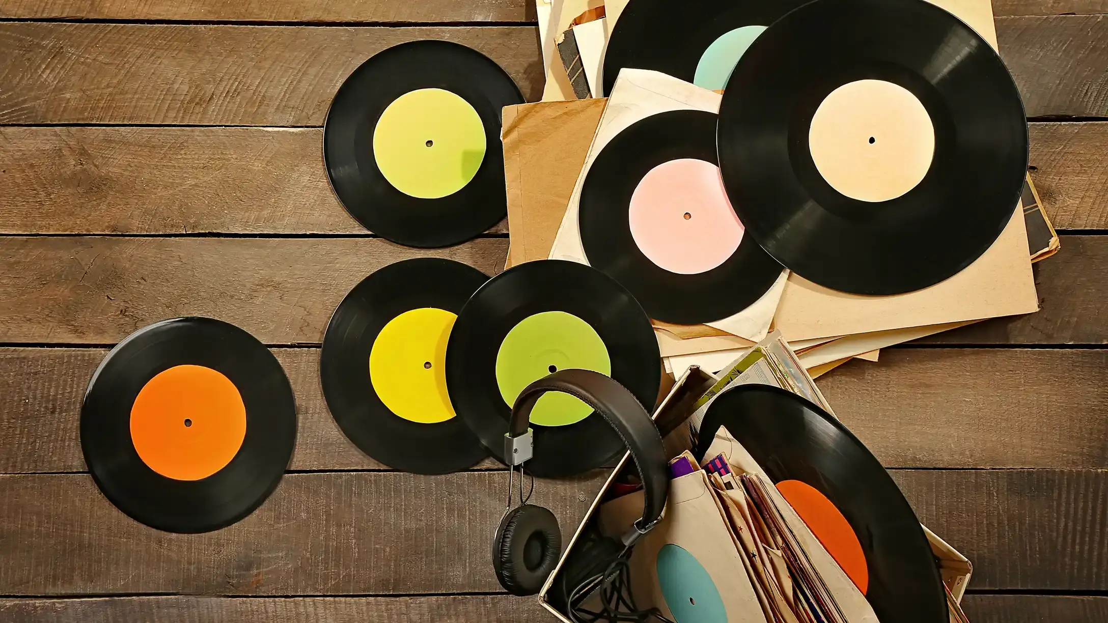 Scattered records and a box of records with a headset, on a wooden floor from a birdseye view