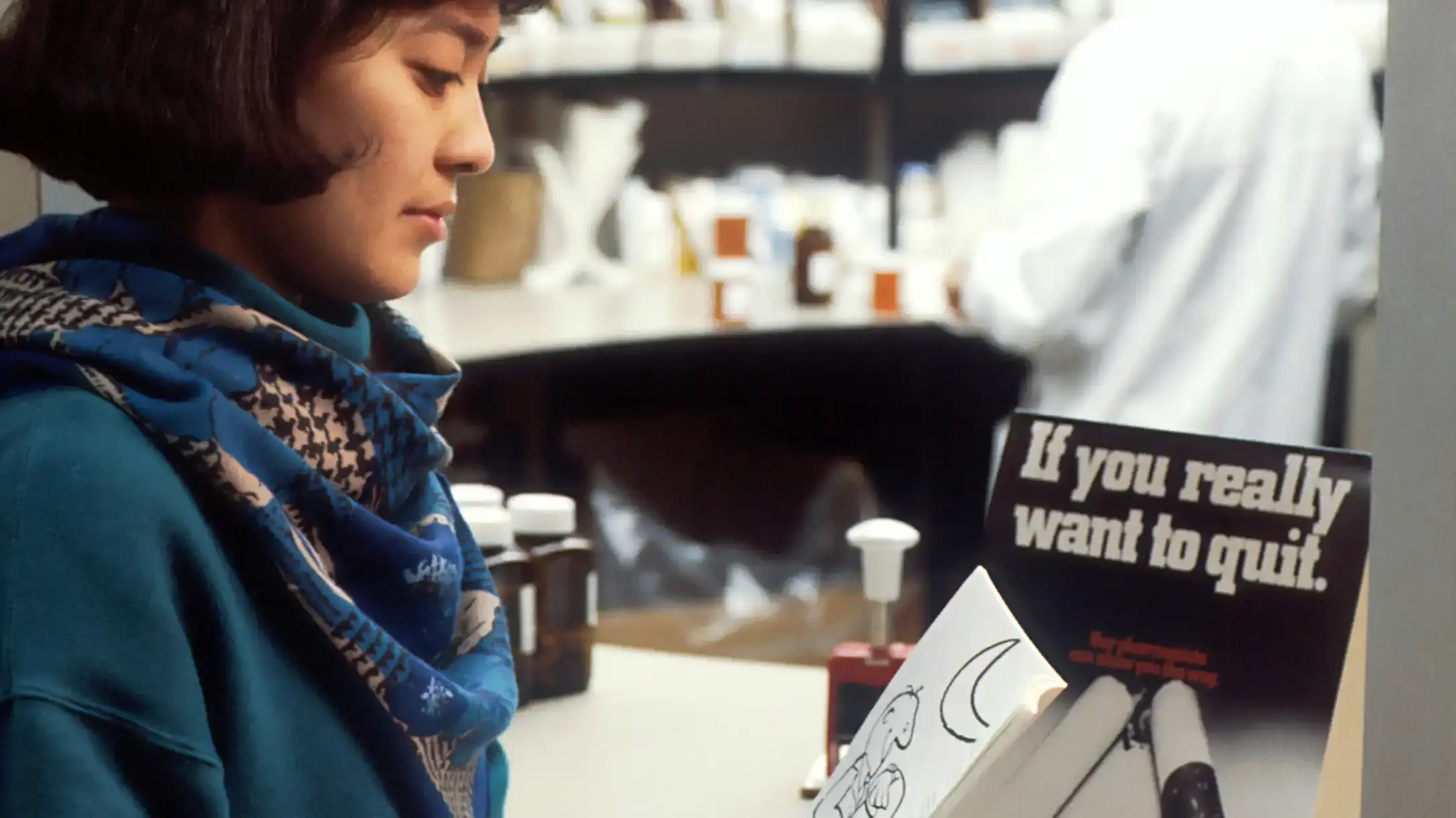 A woman stands in a pharmacy reading a 'quit smoking' leaflet