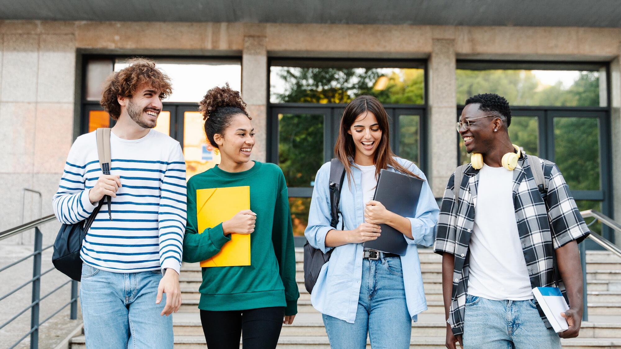 Four students walking out of a building carrying bags and books