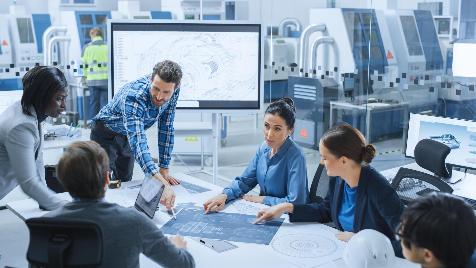 People around a meeting table looking at schematics