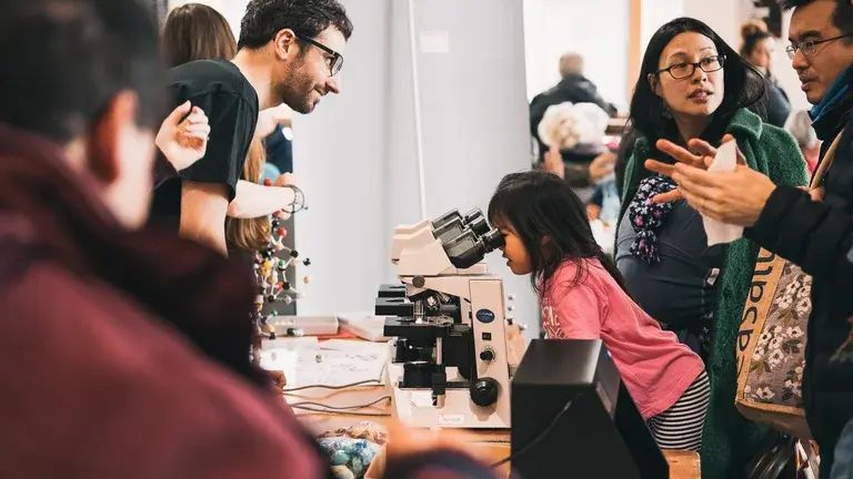 A young girl looking through a microscope at a public engagement event