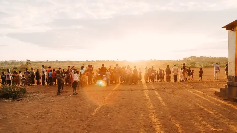 Adults and children stand in front of sun that is setting on horizon and casting a golden light over the foreground