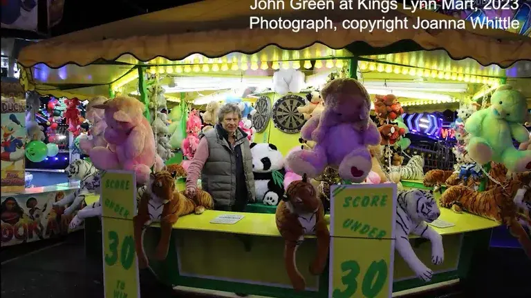 Showman John Green standing in his fairground round stall