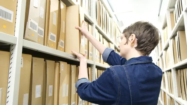 A woman in a room filled with archived folders, taking one of them out.