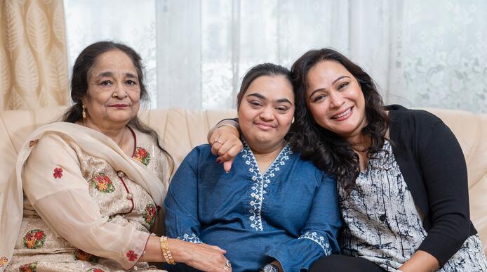 A woman sits between her mother and grandmother on a sofa