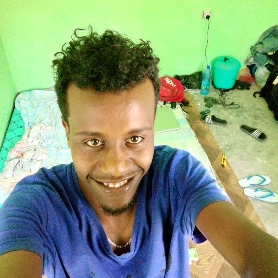 A selfie of Henock, a young man in a blue t-shirt in small green room