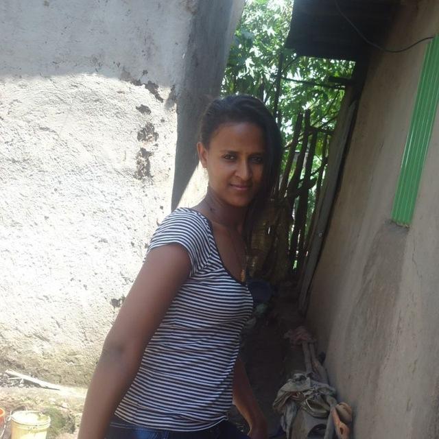 Terefu, a young woman wearing a blue and white striped top stands in an alleyway between to houses
