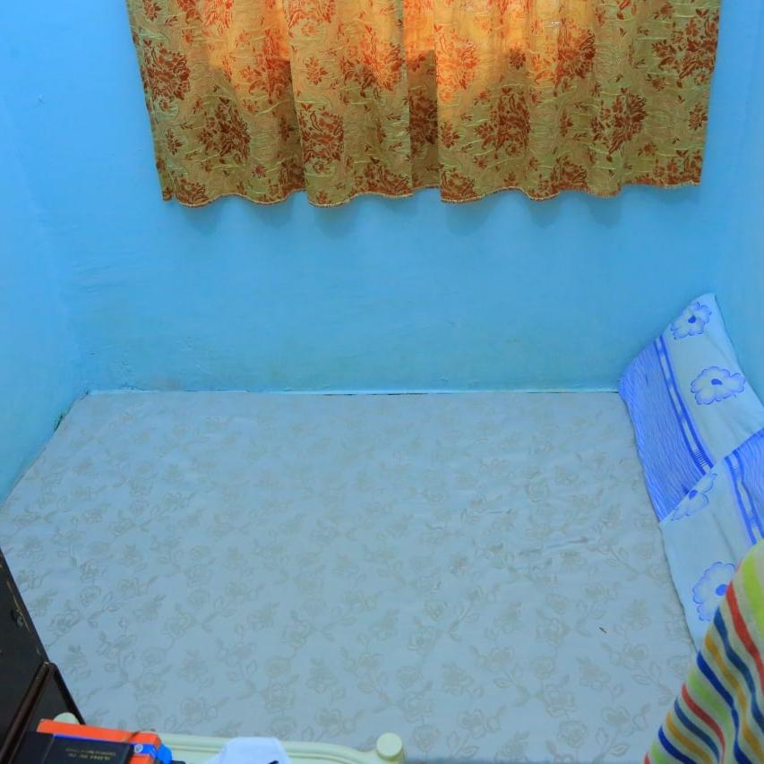 A small mattress on the floor under a window in a small bedroom with light blue walls and patterned orange curtains