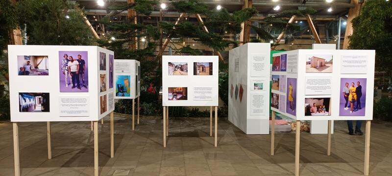 Four white, square exhibition boards displaying photographs of you Ethiopian and south African people in their homes