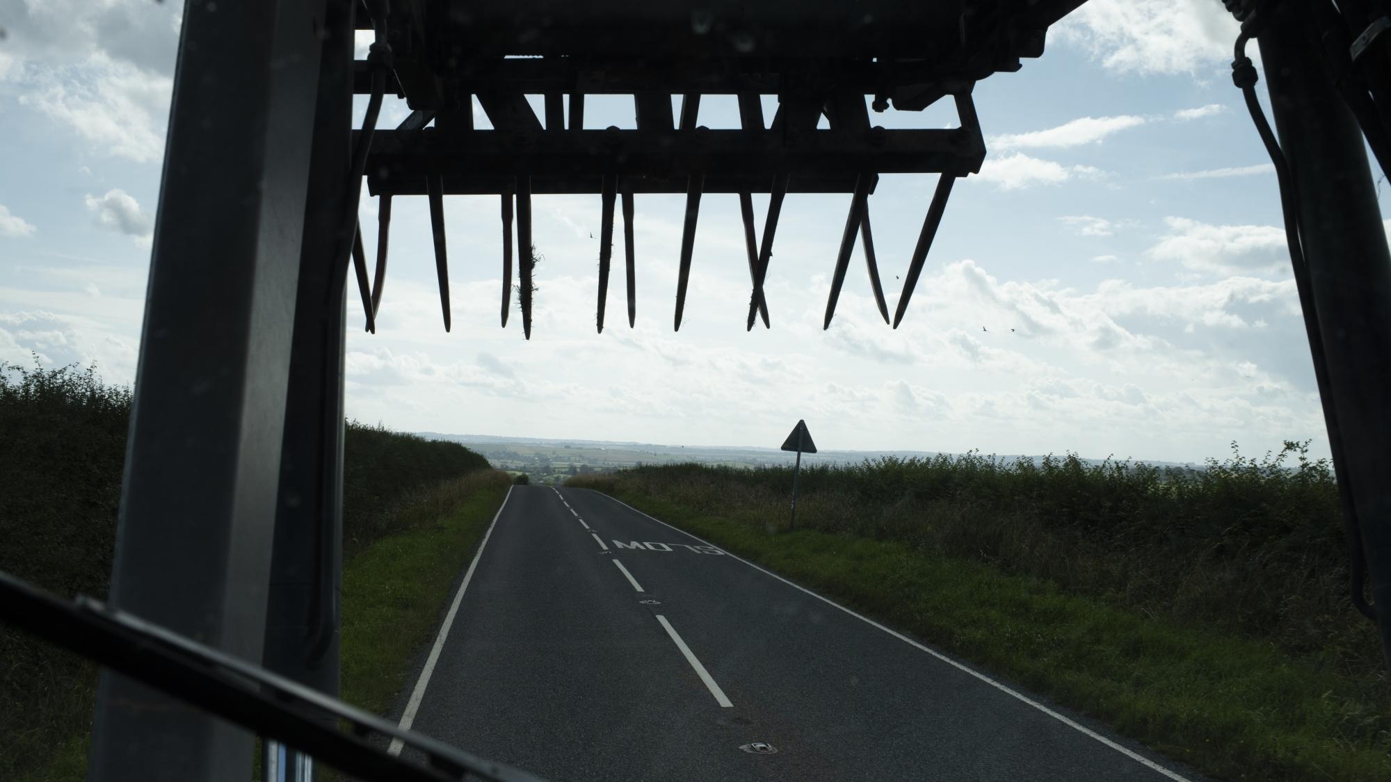 View out the windscreen of a tractor driving down a country road