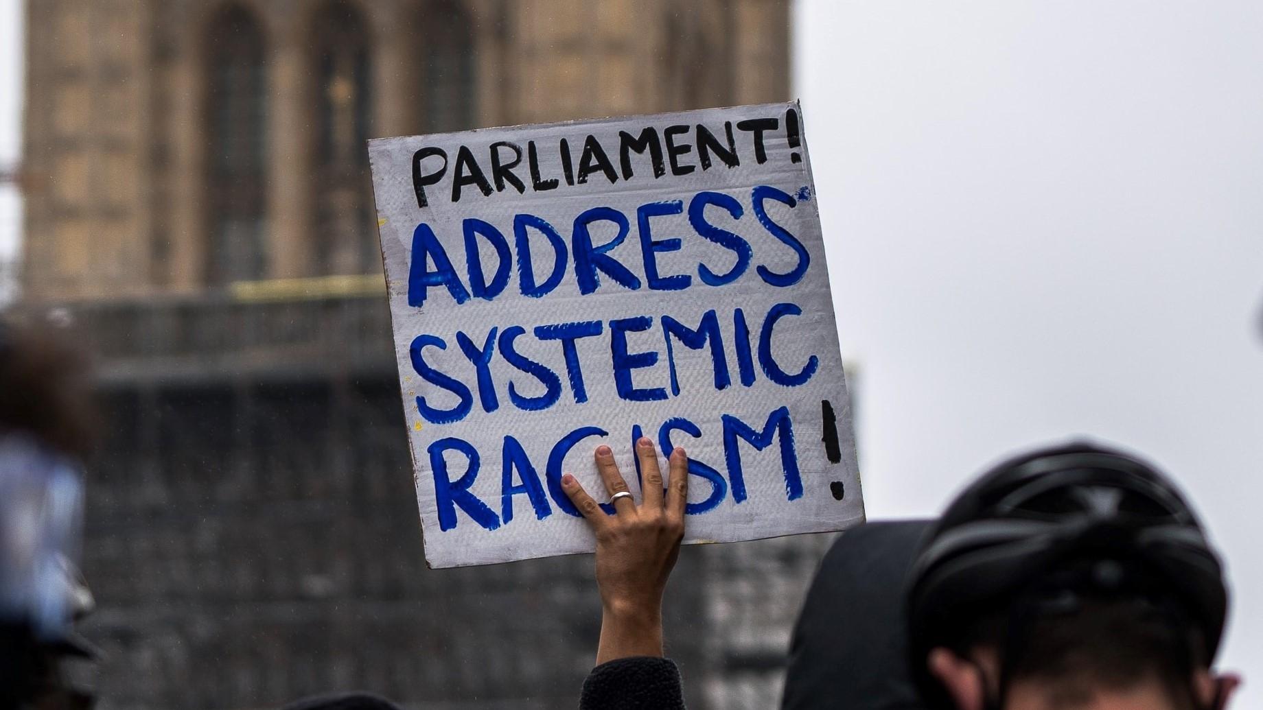 Protest sign stating 'Parliament! Address systemic racism!'