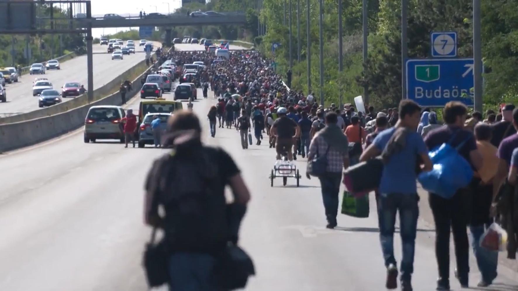 Film still of refugees travelling down a road