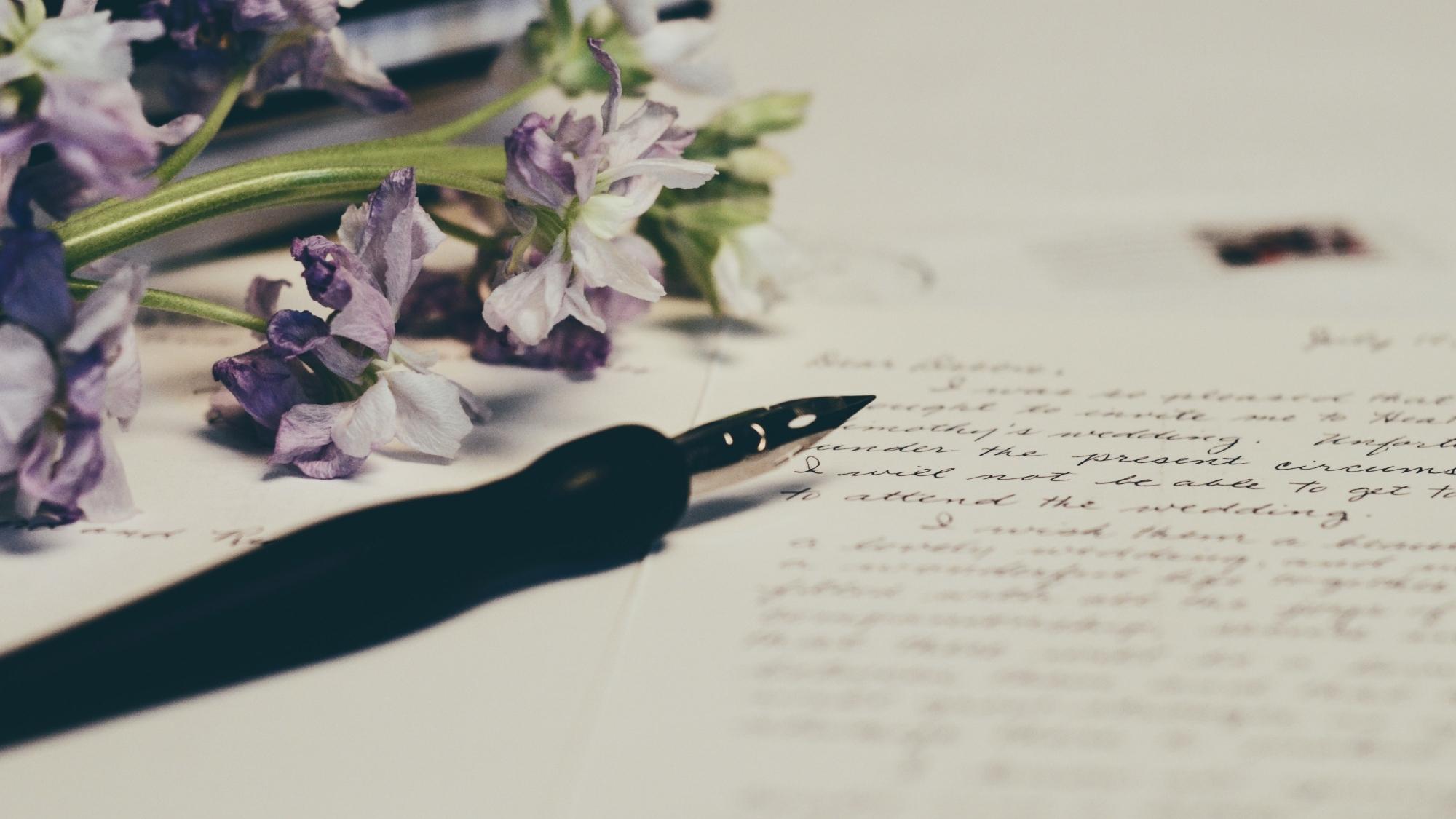 A handwritten letter with a fountain pen and purple flowers