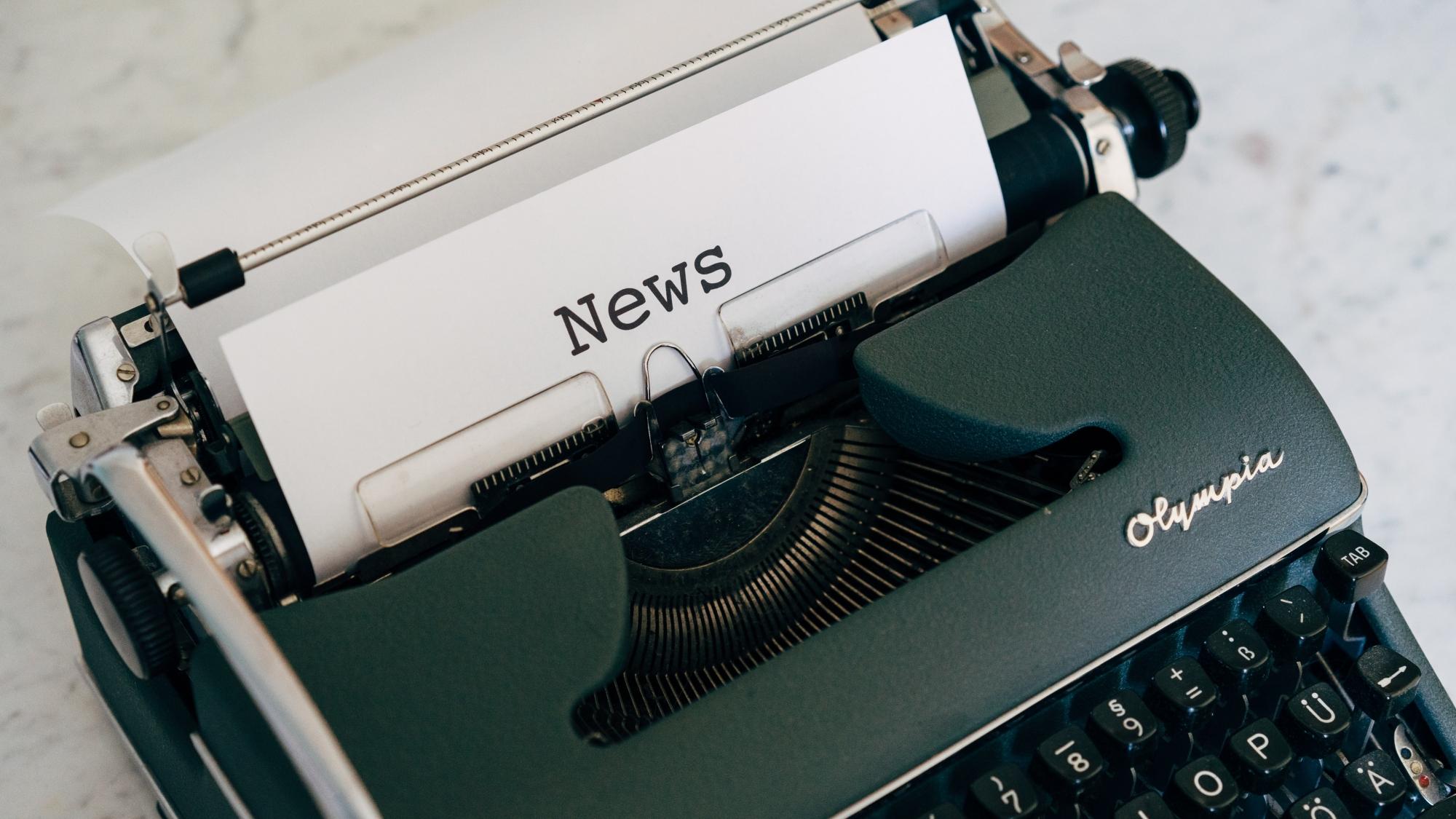 A green typewriter with a piece of paper loaded into it, the word 'News' has been typed at the top of the paper