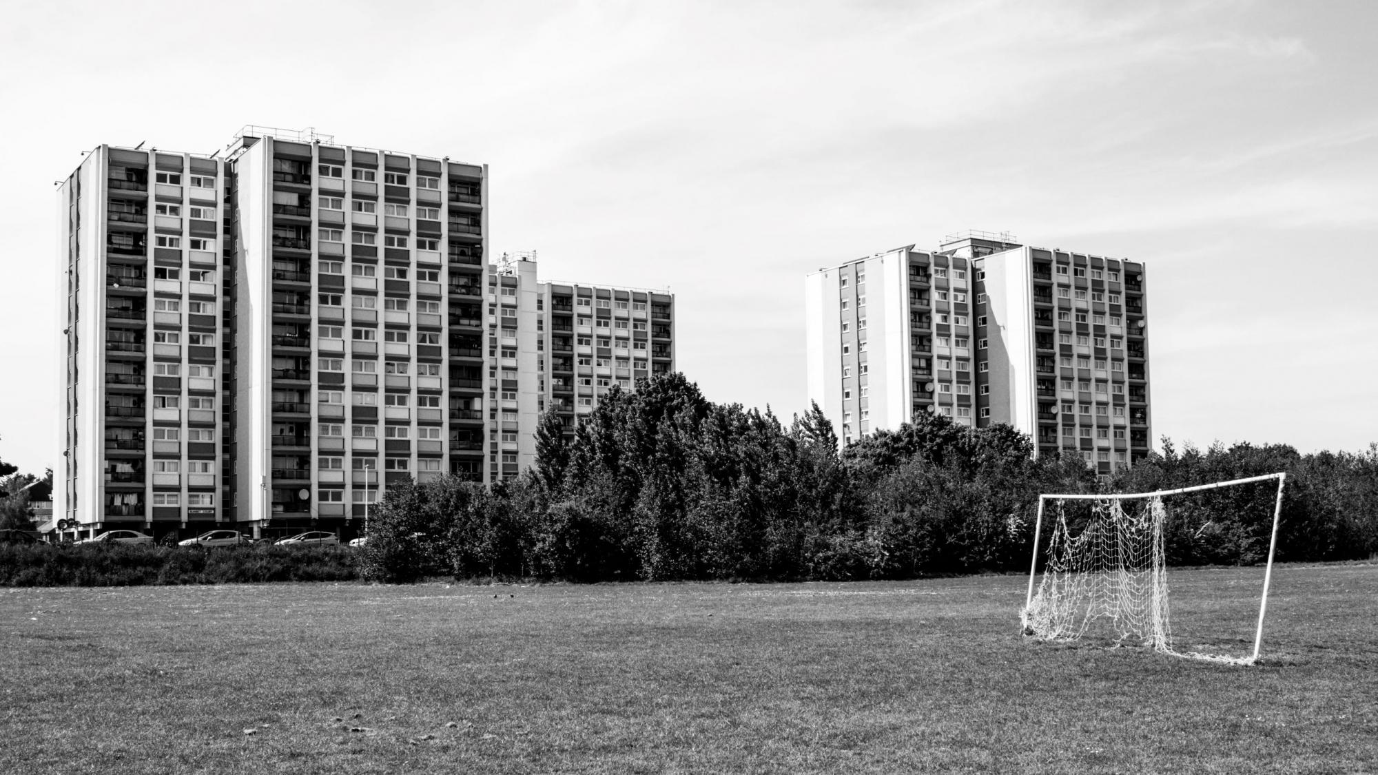 Black and white image of a playing field in front of three blocks of flats