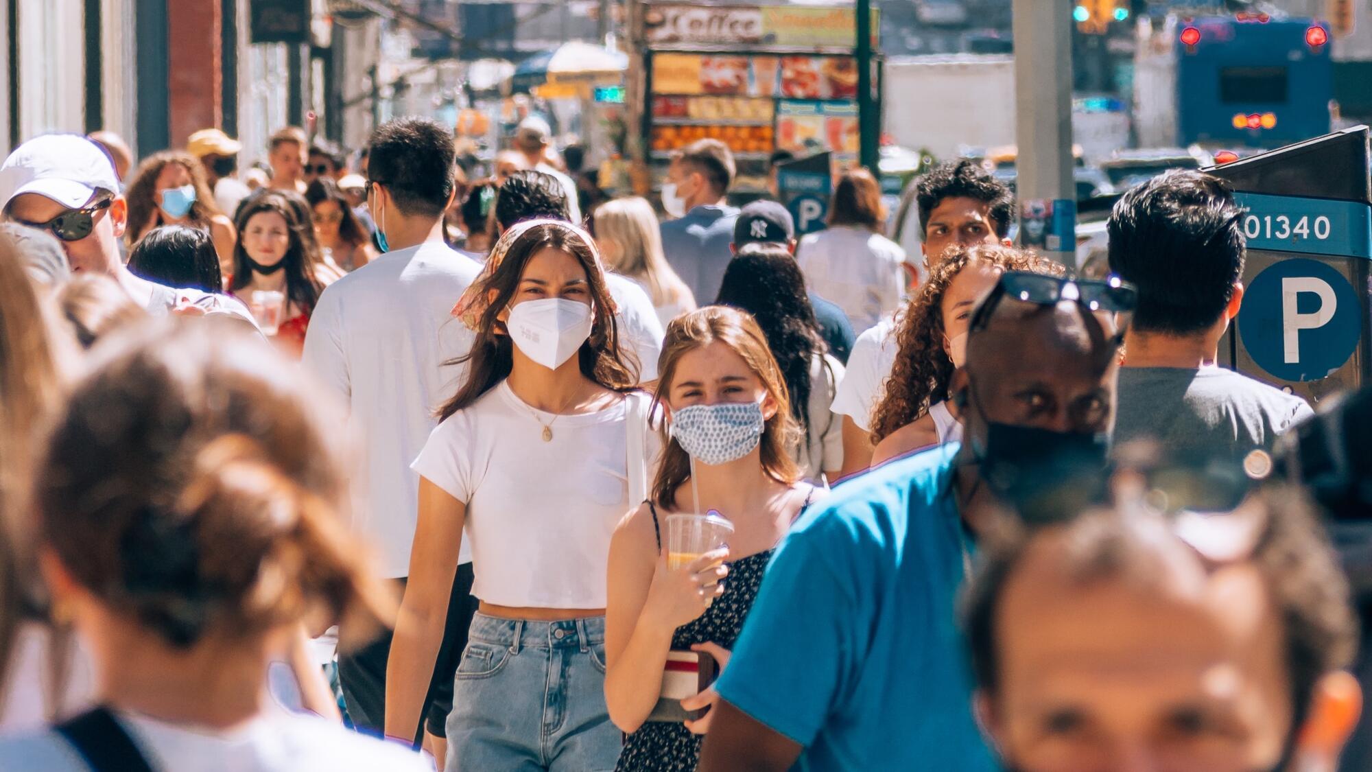 A crowd of people walking through a city street wearing medical masks