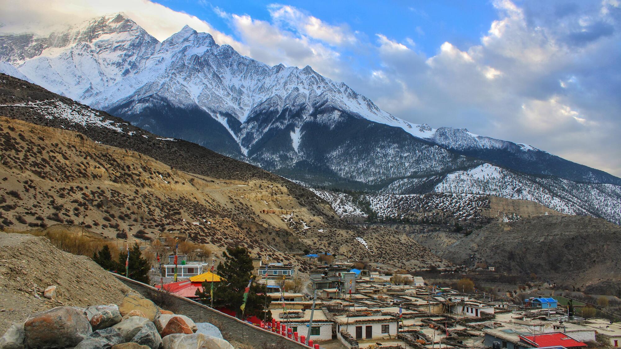 A settlement in Nepal beneath a snow-topped mountain range