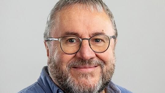 a picture of peter coffey, a white man with a beard, wearing glasses and a blue shirt