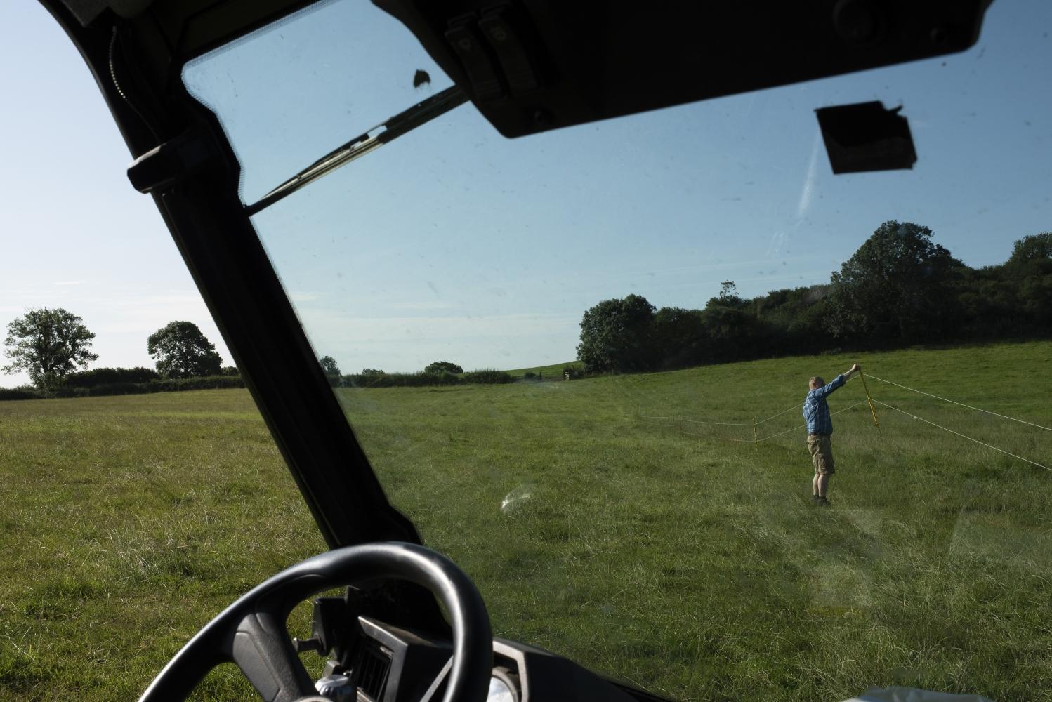 View of a man installing an electric fence out the windscreen of a tractor