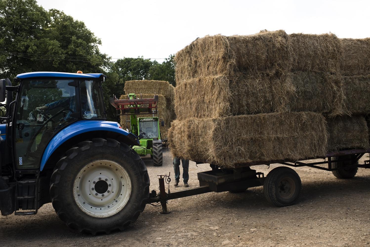 A tractor pulling a trailer of hay stacks