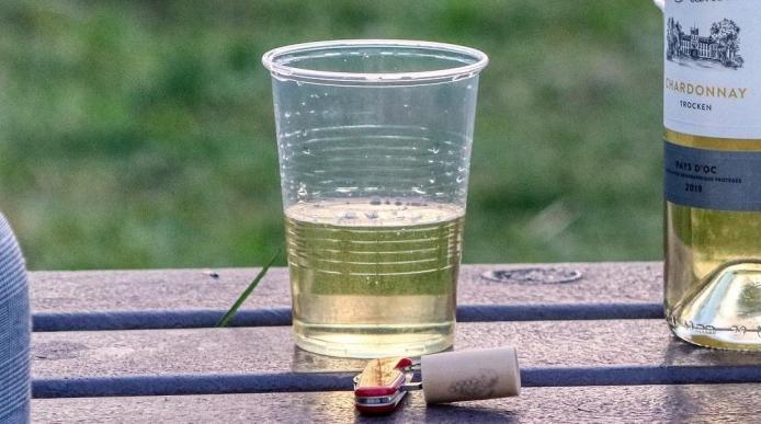 A bottle of wine with two plastic cups on a bench outdoors