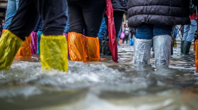 People walking through a flooded area with plastic coverings around their legs and feet
