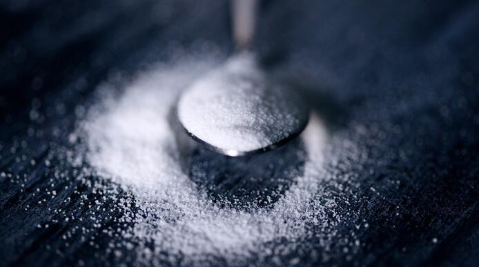 A teaspoon of white sugar placed on a surface top