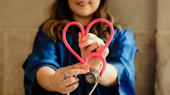 A health care professional holding out a stethoscope in the shape of a love heart