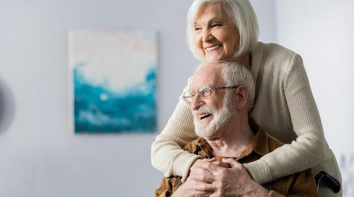 A cheerful elderly woman embracing an elderly man in a wheelchair