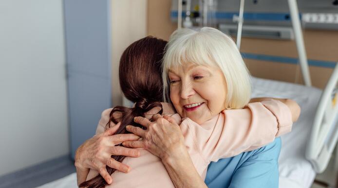 An elderly women in a care facility hugging a younger woman 