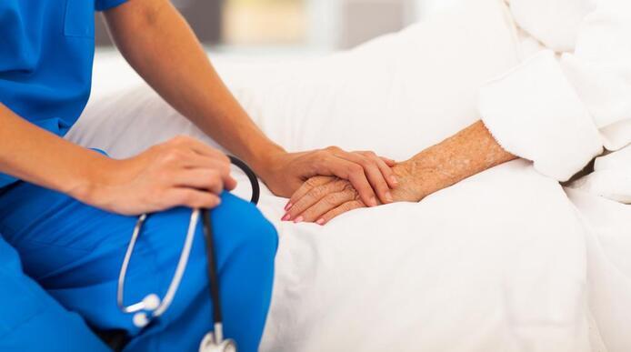 A caregiver holding the hand of an elderly patient lying in bed