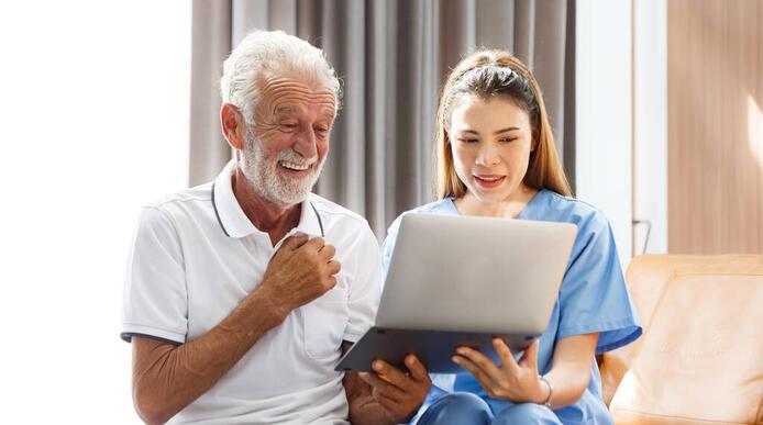 A female careworker sat beside an elderly man, looking at a laptop together