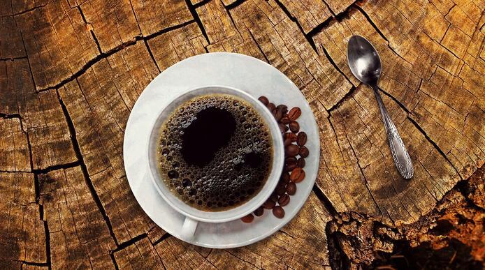 a picture of a cup of coffee and some coffee beans on a wooden table 