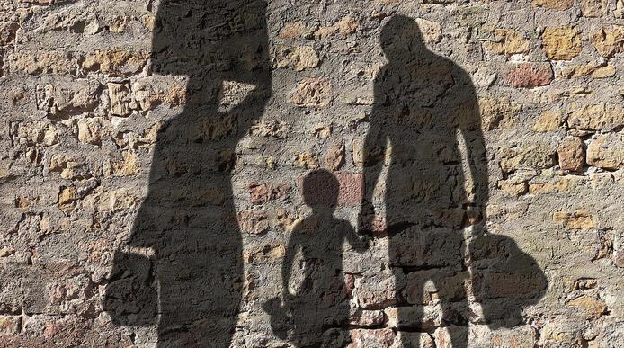 Shadow on a stone wall of a man, woman and child carrying luggage 