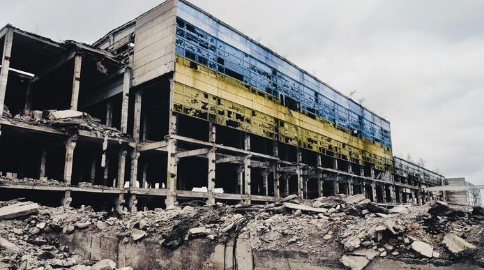 The ruins of a concrete building, with the blue and yellow Ukrainian flag painted on the front